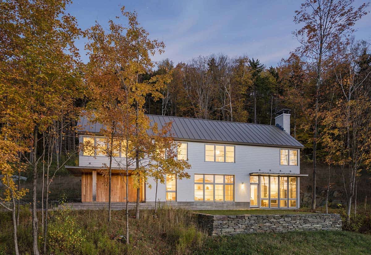 Lit home at dusk with cedar-clad entry and dry-stacked stone wall