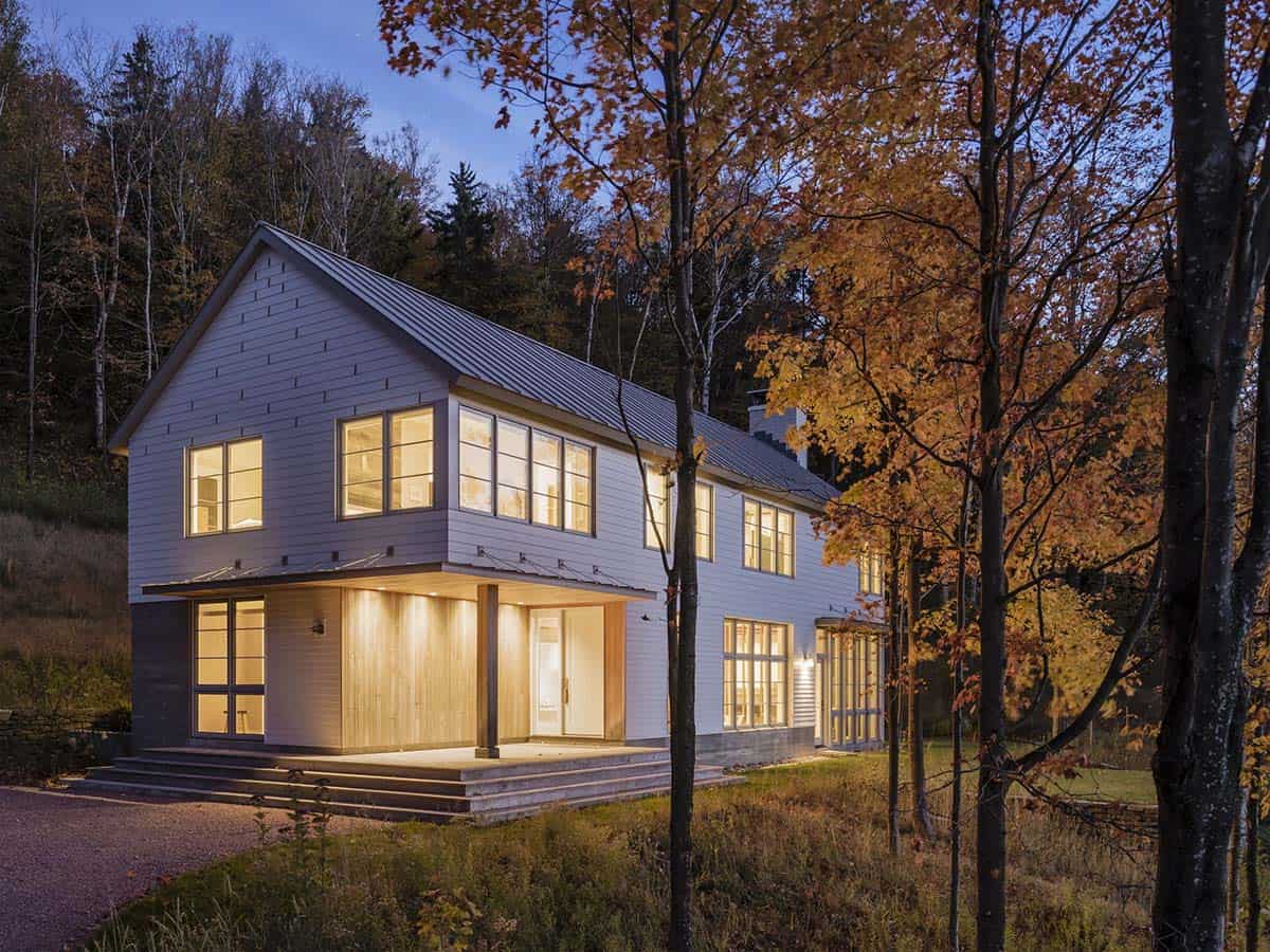 Entry porch with wood-clad wall and glowing windows among autumn trees