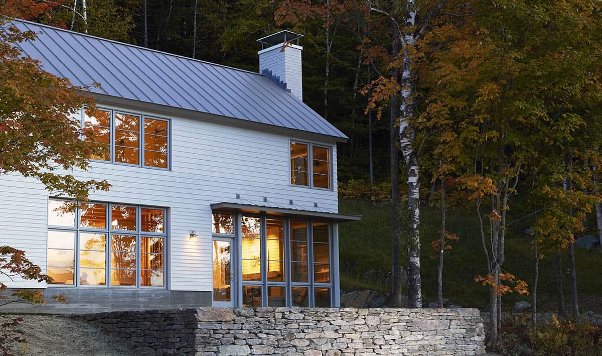 Warmly lit windows and metal roof above a dry-stacked stone wall