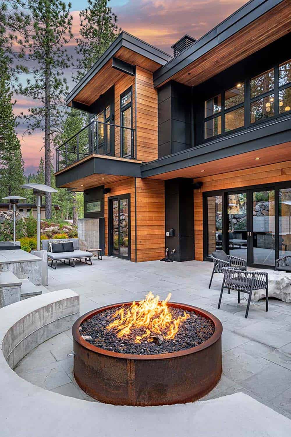 Corten steel fire pit on a bluestone patio with a curved concrete bench beside the cedar-clad home