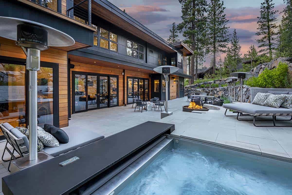 Hot tub and heated patio at dusk with outdoor heaters, lounge chairs, and a fire pit beside sliding glass doors