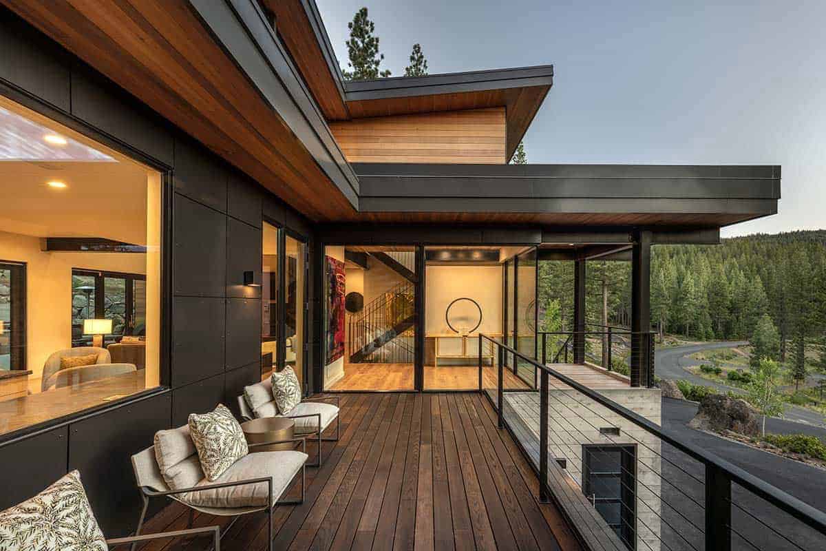 Covered wood deck with outdoor lounge chairs and cable railing overlooking the forest and winding road