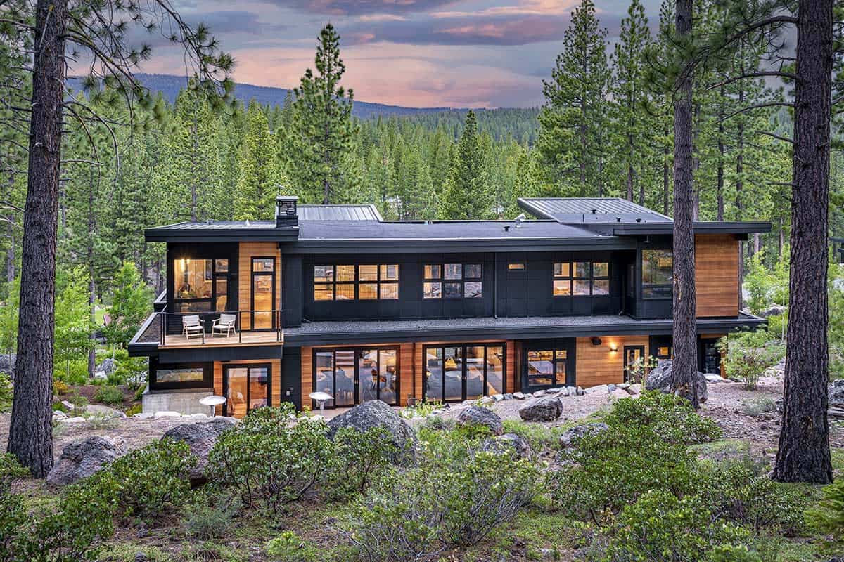 Back of the home seen through pine trees, with a small upper balcony and walls of sliding glass doors