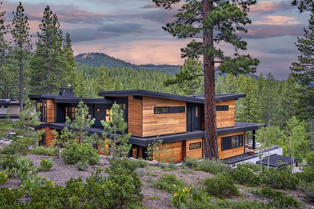 Side view of the home with flat sloping roofs, cedar siding, and forested mountain beyond