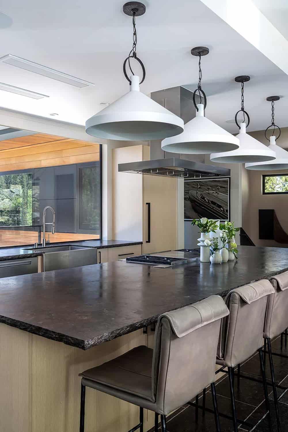 Kitchen island with a rough-edged stone countertop, leather barstools, and white conical pendant lights