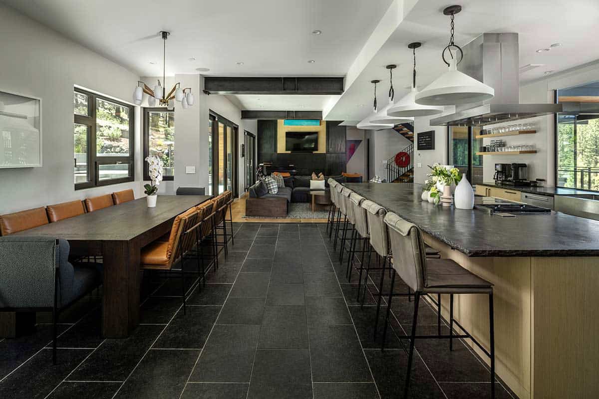 Open kitchen, dining, and living area with a long island, wood dining table, and dark stone floor