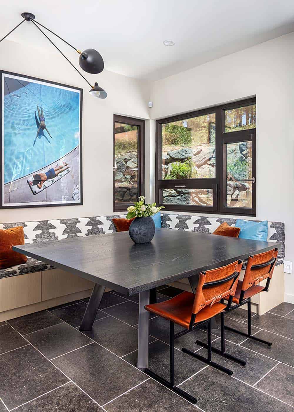 Breakfast nook with a built-in patterned banquette, dark table, rust leather chairs, and a large pool photograph