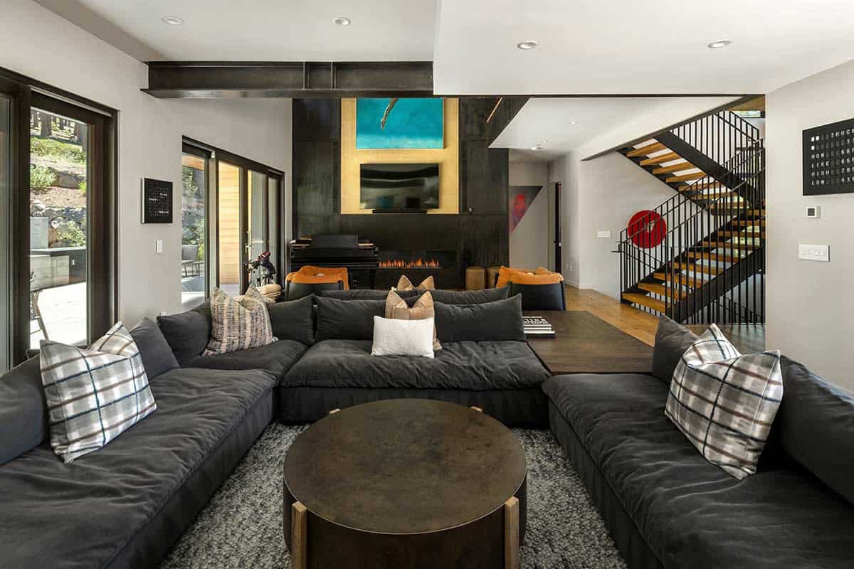 Living room with a charcoal sectional, round bronze coffee table, and open-tread staircase
