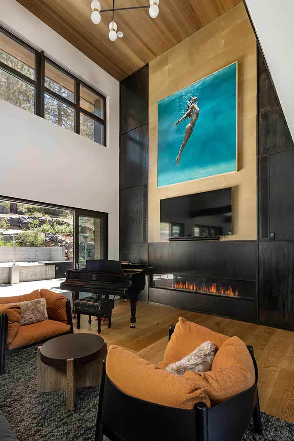 Two-story living room with a steel and gold-leaf fireplace wall, underwater painting, grand piano, and orange armchairs