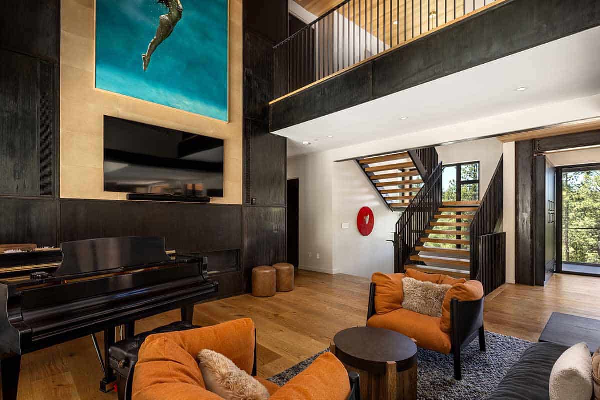 Living area with a black steel fireplace wall, grand piano, loft overlook, and floating wood stairs