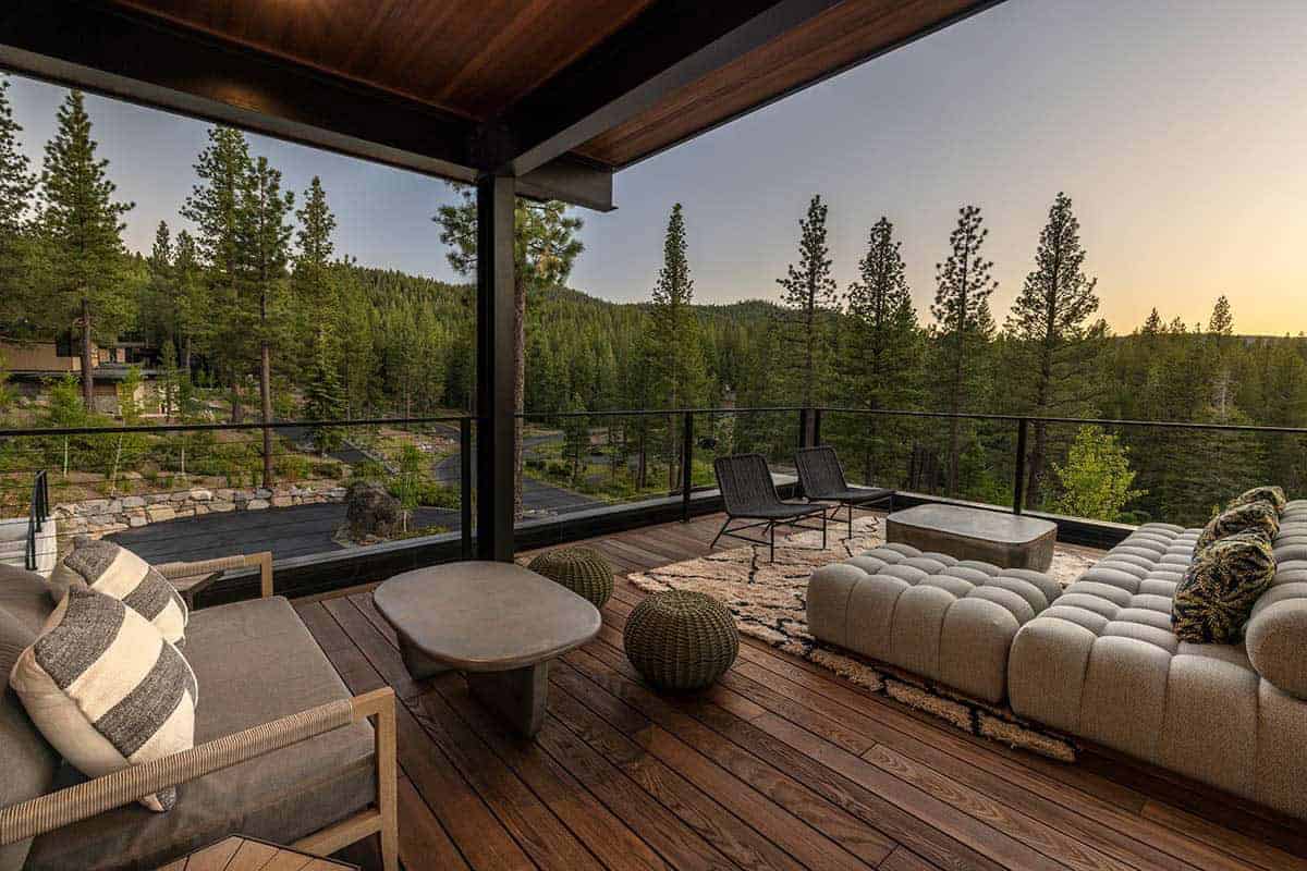 Covered upper deck with cushioned sofas, a patterned rug, and sunset views over the pine forest