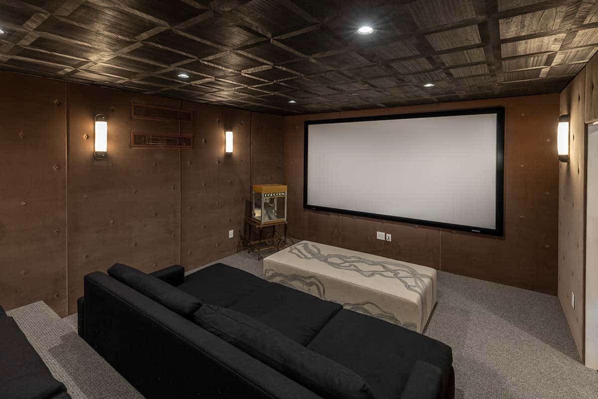 Home theater with a large projection screen, black sectional, coffered dark wood ceiling, and a vintage popcorn machine