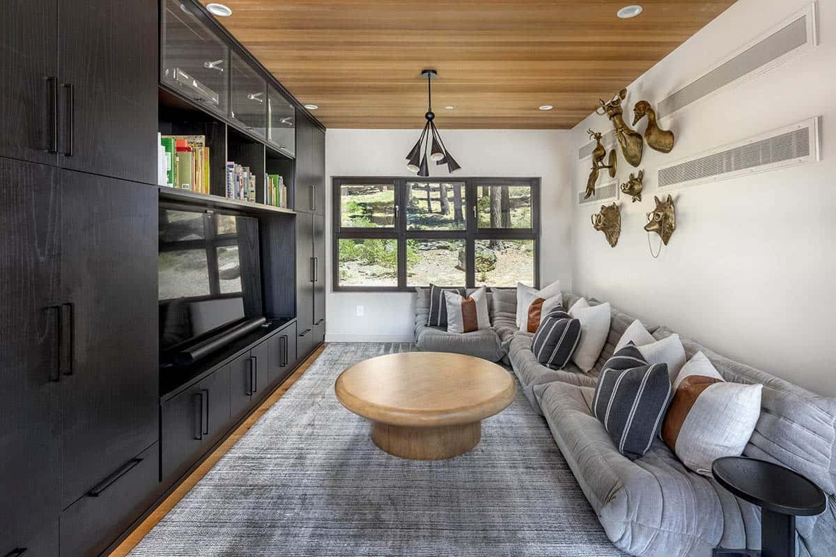 Cozy media room with a black built-in wall unit, gray floor sofa, round wood coffee table, and brass animal wall decor