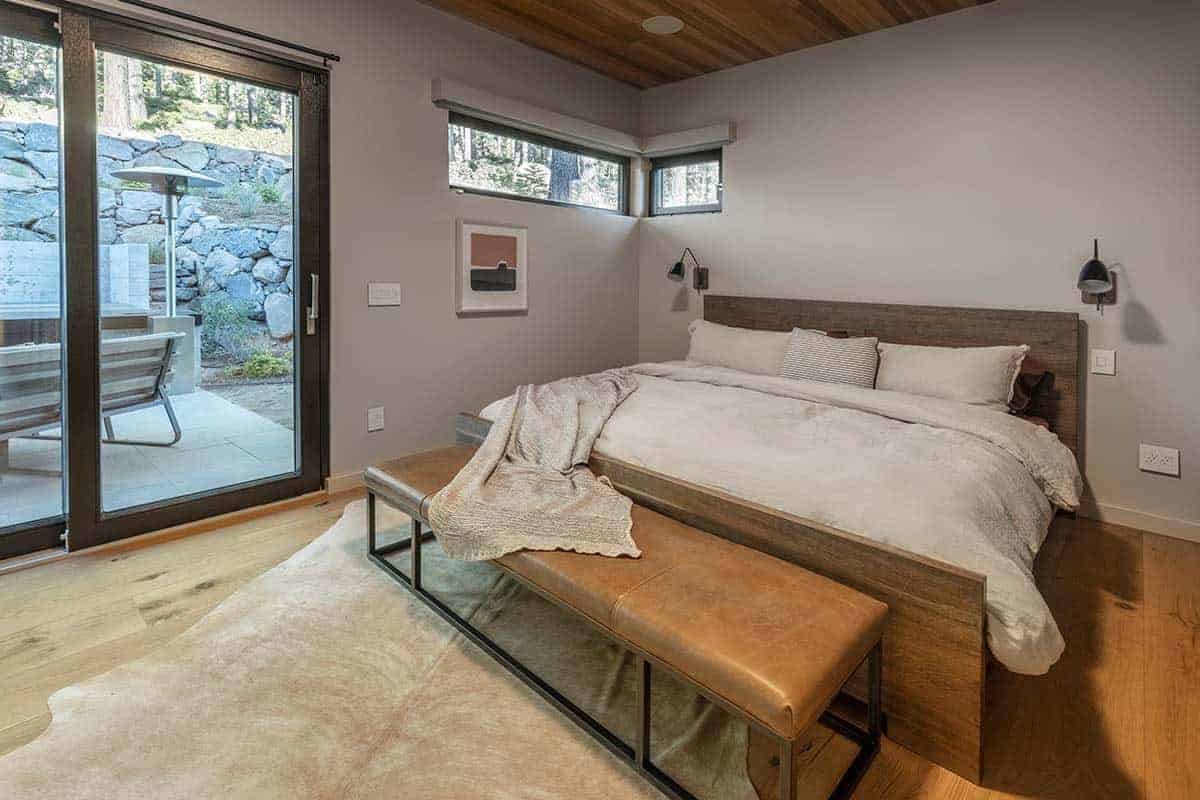 Guest bedroom with a wood-framed bed, a leather bench, a cowhide rug, and sliding glass doors to the patio