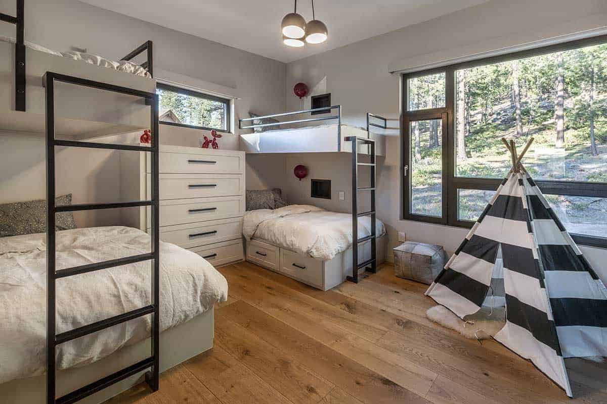 Kids' bunk room with built-in bunks, a drawer chest, and a black-and-white striped teepee by a forest-view window