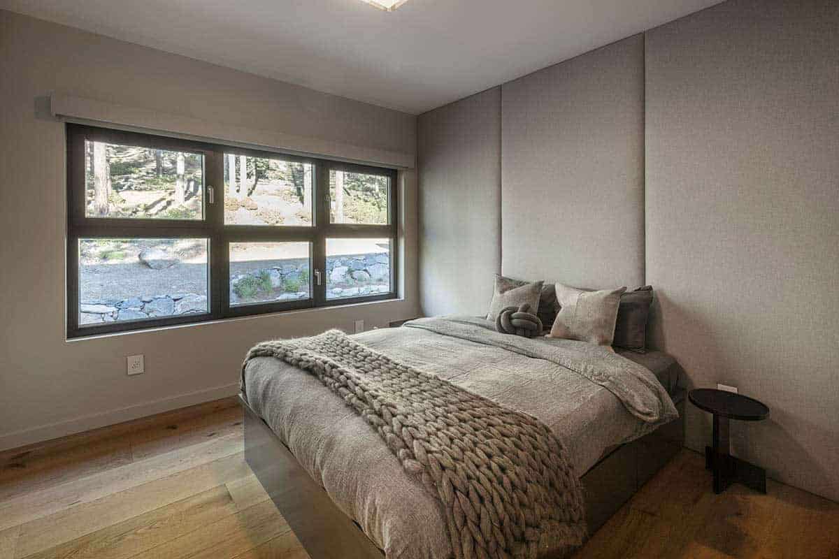 Bedroom with a padded gray wall panel headboard, a chunky knit throw, and a wide window overlooking the rocky hillside