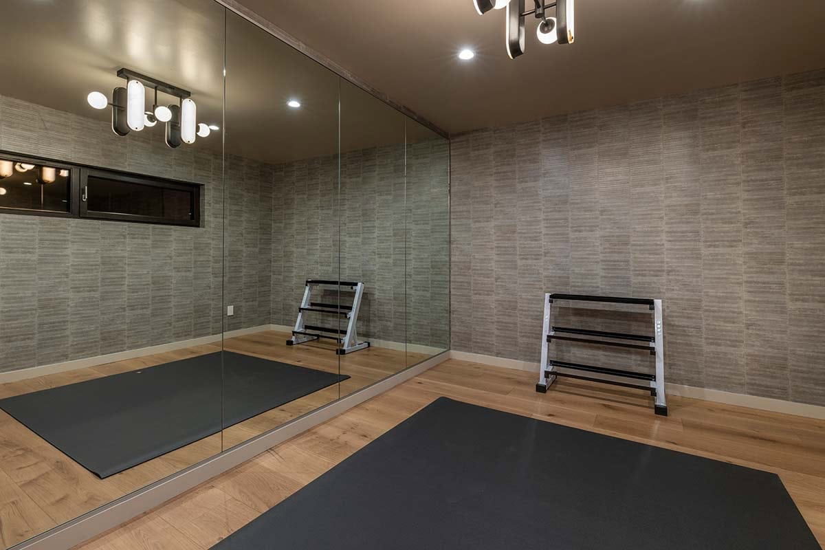 Home gym with a mirrored wall, dumbbell racks, black floor mats, and light wood flooring