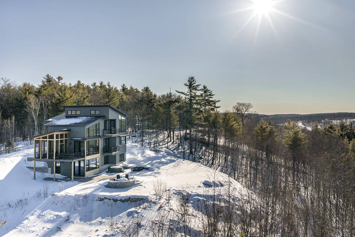Three-story gray modern home with a screened porch on a snowy hilltop in low winter sun
