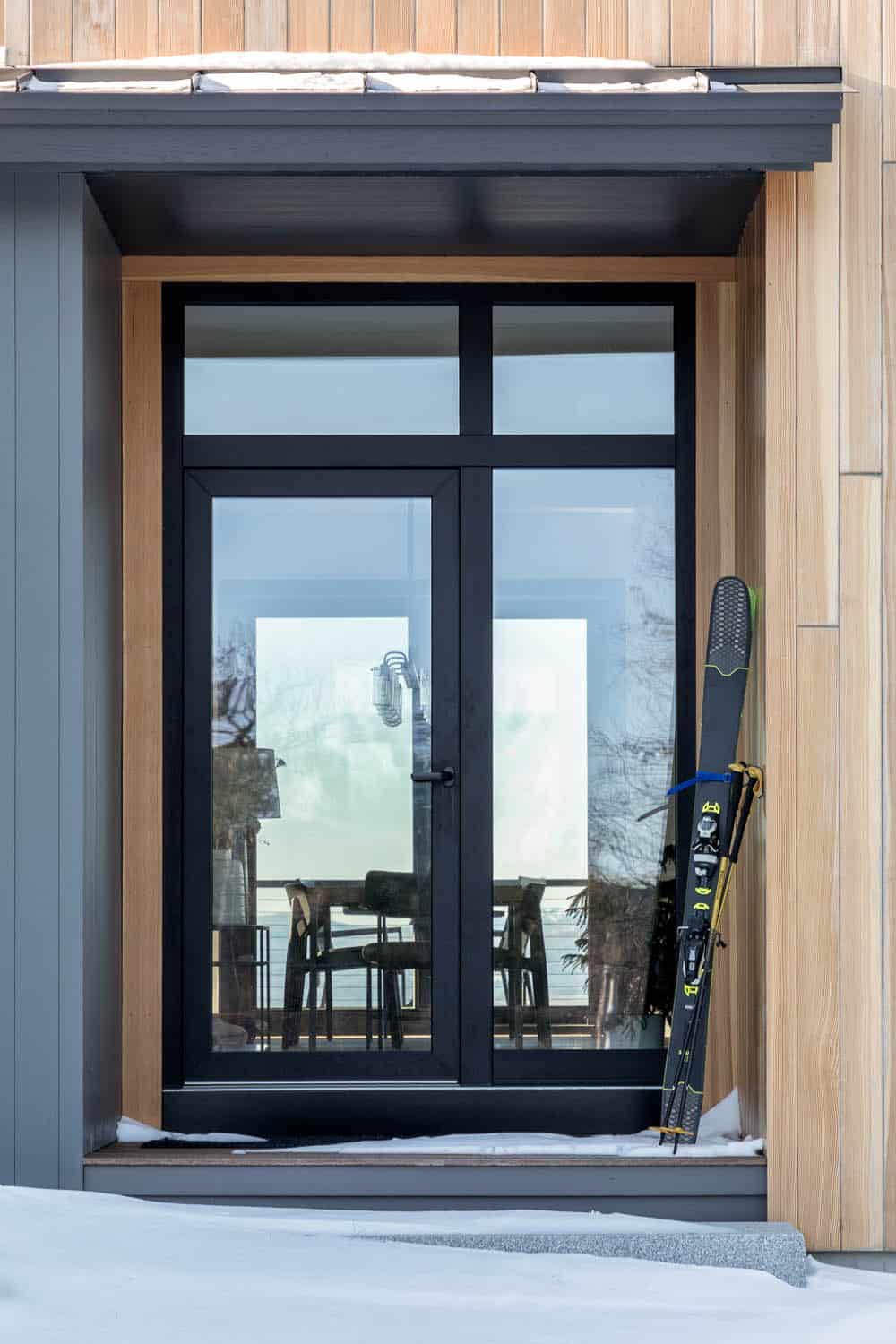 Black-framed double doors in a cedar-lined entry with a ski and poles leaning beside them