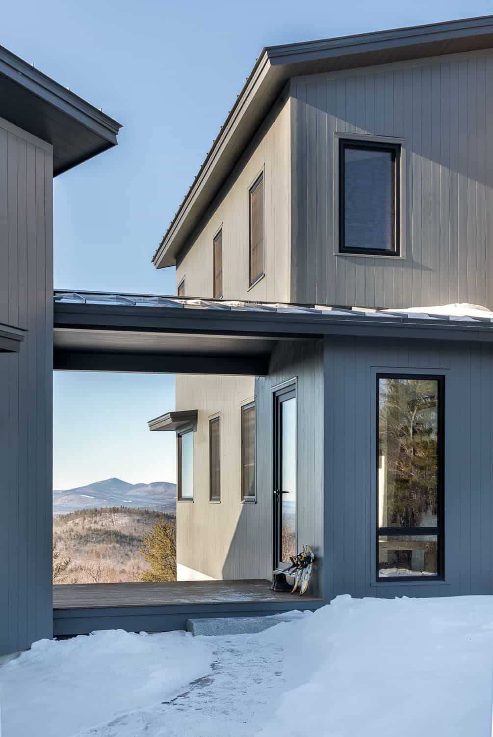 Covered breezeway between two gray buildings framing a mountain view, with snowshoes by the side door