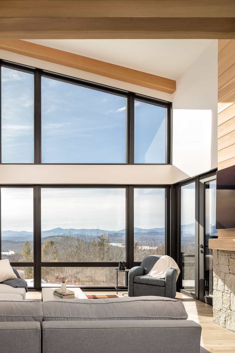 Living room wall of windows framing mountain views beneath a sloped, beamed ceiling