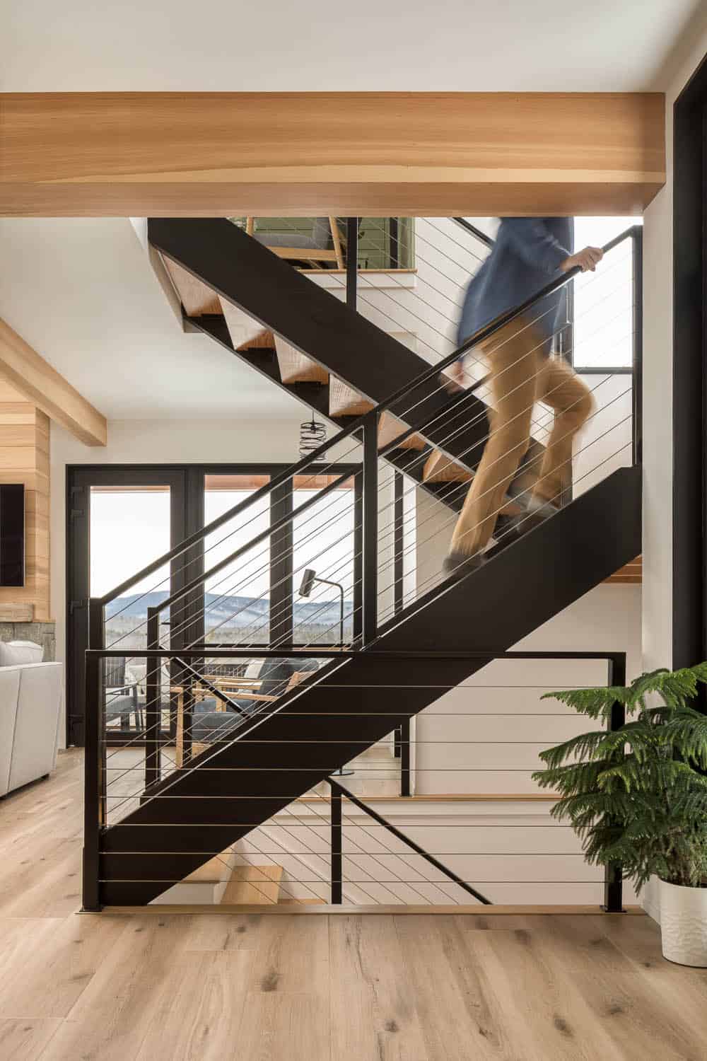 Open steel and wood staircase with cable railings as a person climbs past a potted evergreen