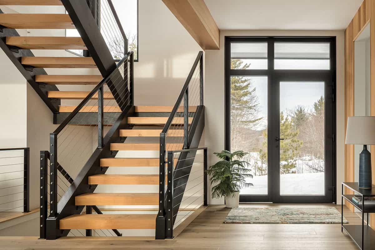 Entry hall with an open-tread wood staircase, cable railings, and a glass door facing snowy pines
