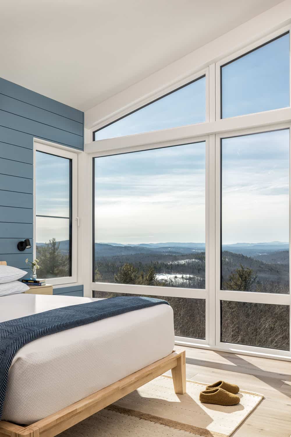 Bedroom with a blue shiplap wall and corner windows overlooking forested hills