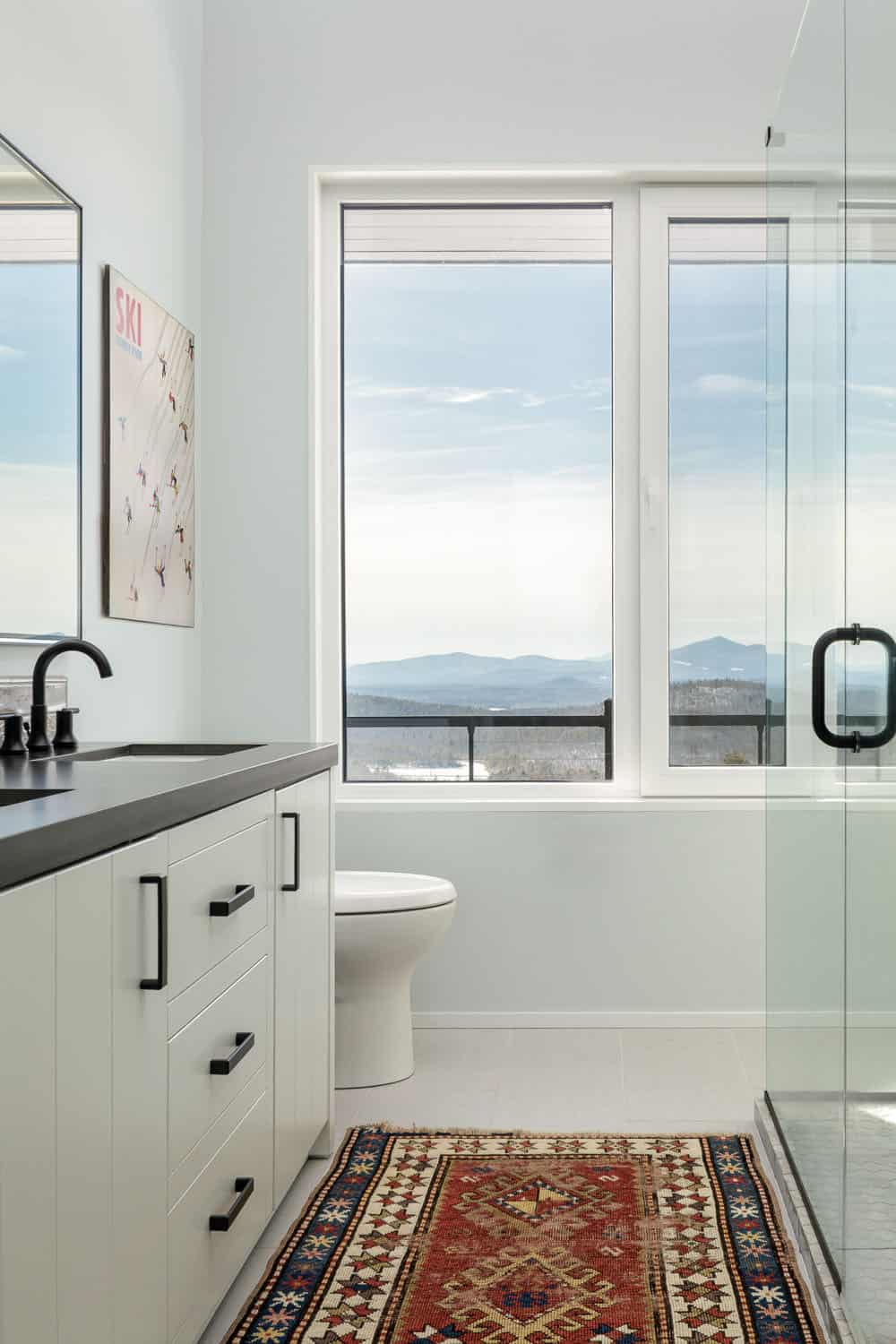 Bathroom with a white vanity, black fixtures, a vintage runner, and a window framing distant mountains