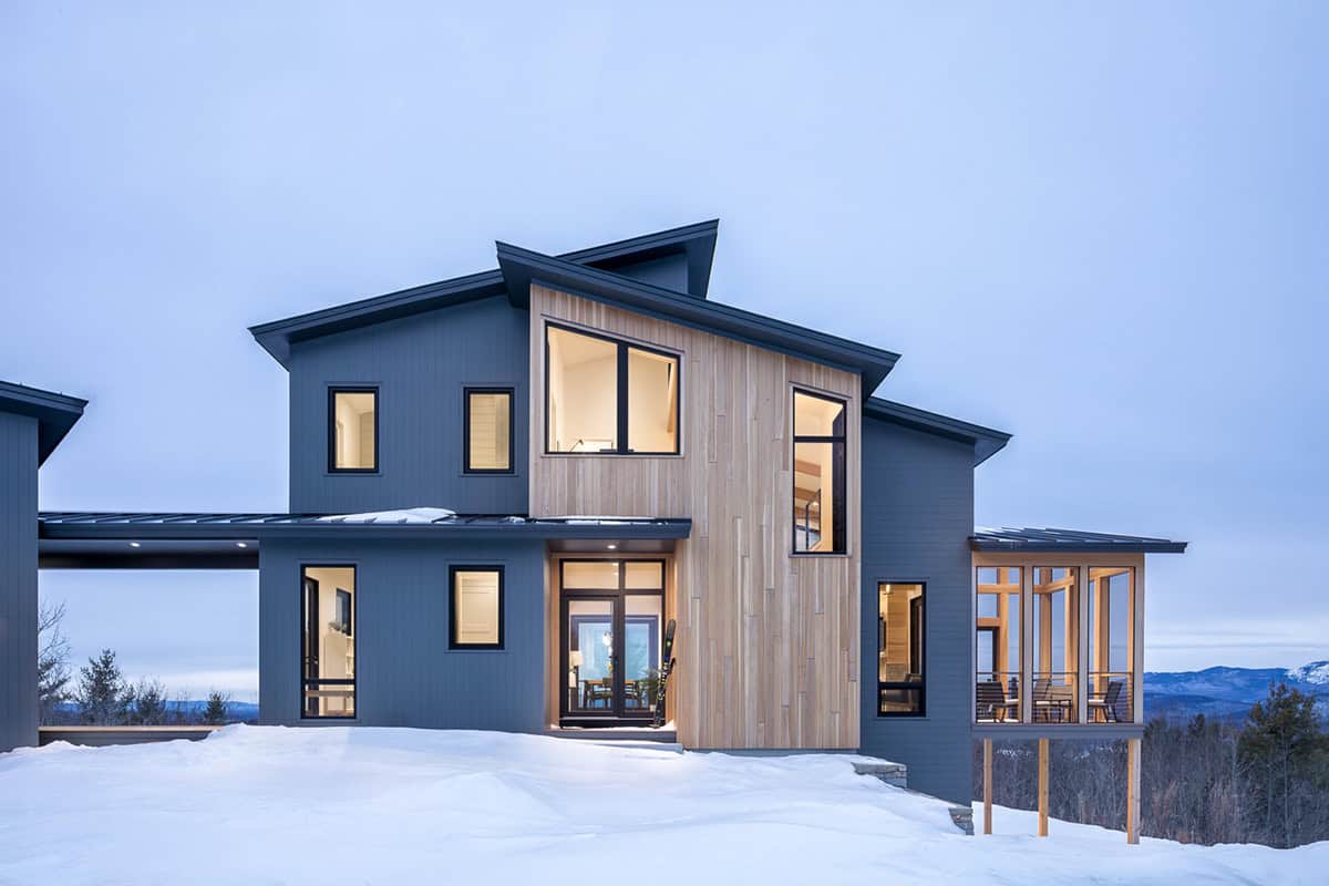 Front facade at twilight with glowing windows, a cedar entry, and a ski by the door