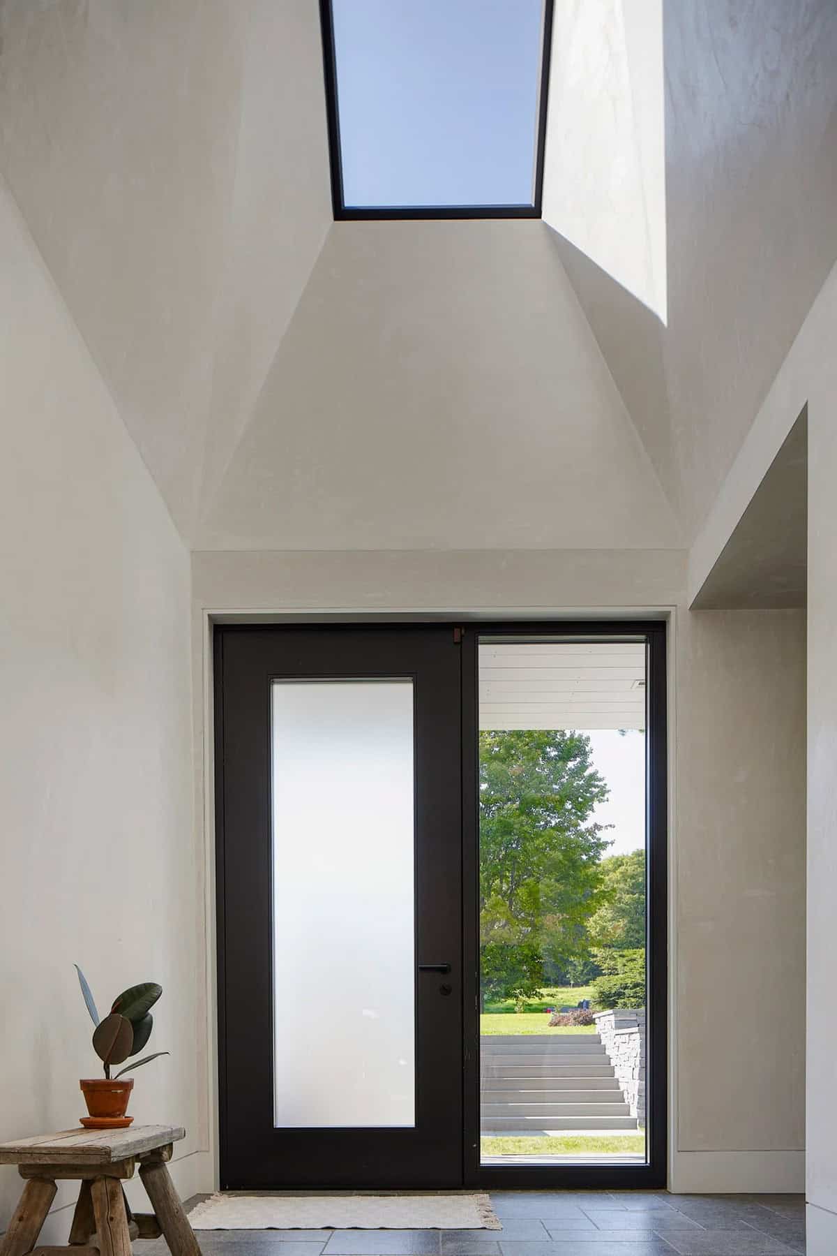 Modern farmhouse entry with black glass door, skylight, and plaster walls