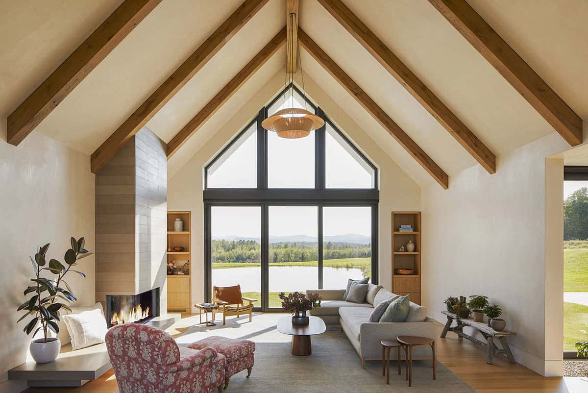 Farmhouse living room with vaulted beamed ceiling, fireplace, and pond view through a gable window