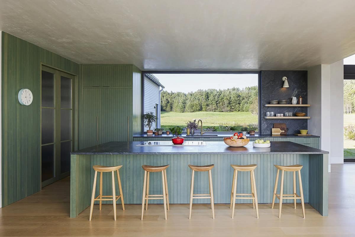 Modern farmhouse kitchen with green paneled island, oak stools, and picture window