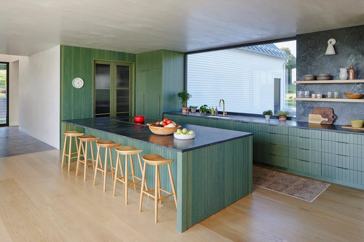 Green kitchen with dark stone countertops, brass faucet, and open shelving