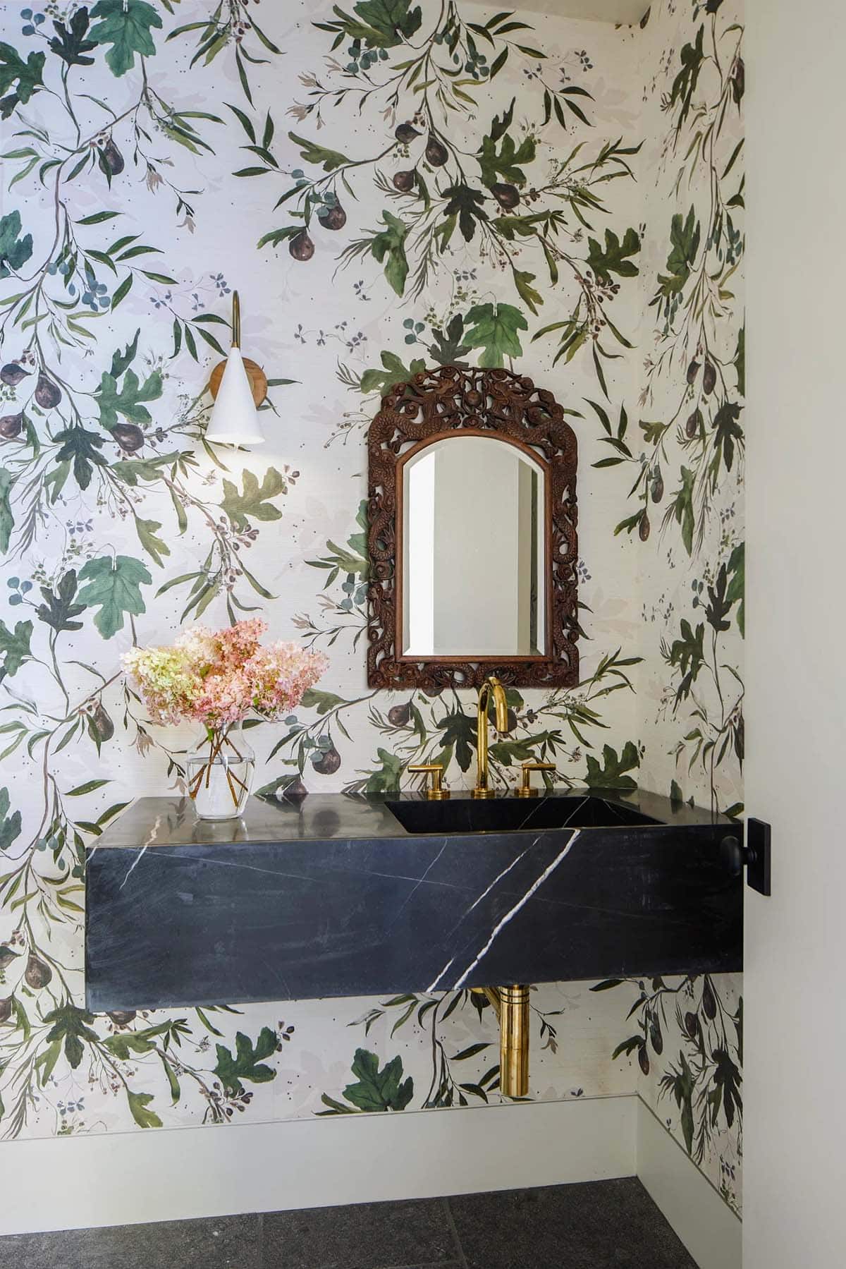 Powder room with fig leaf wallpaper, black stone sink, and brass fixtures