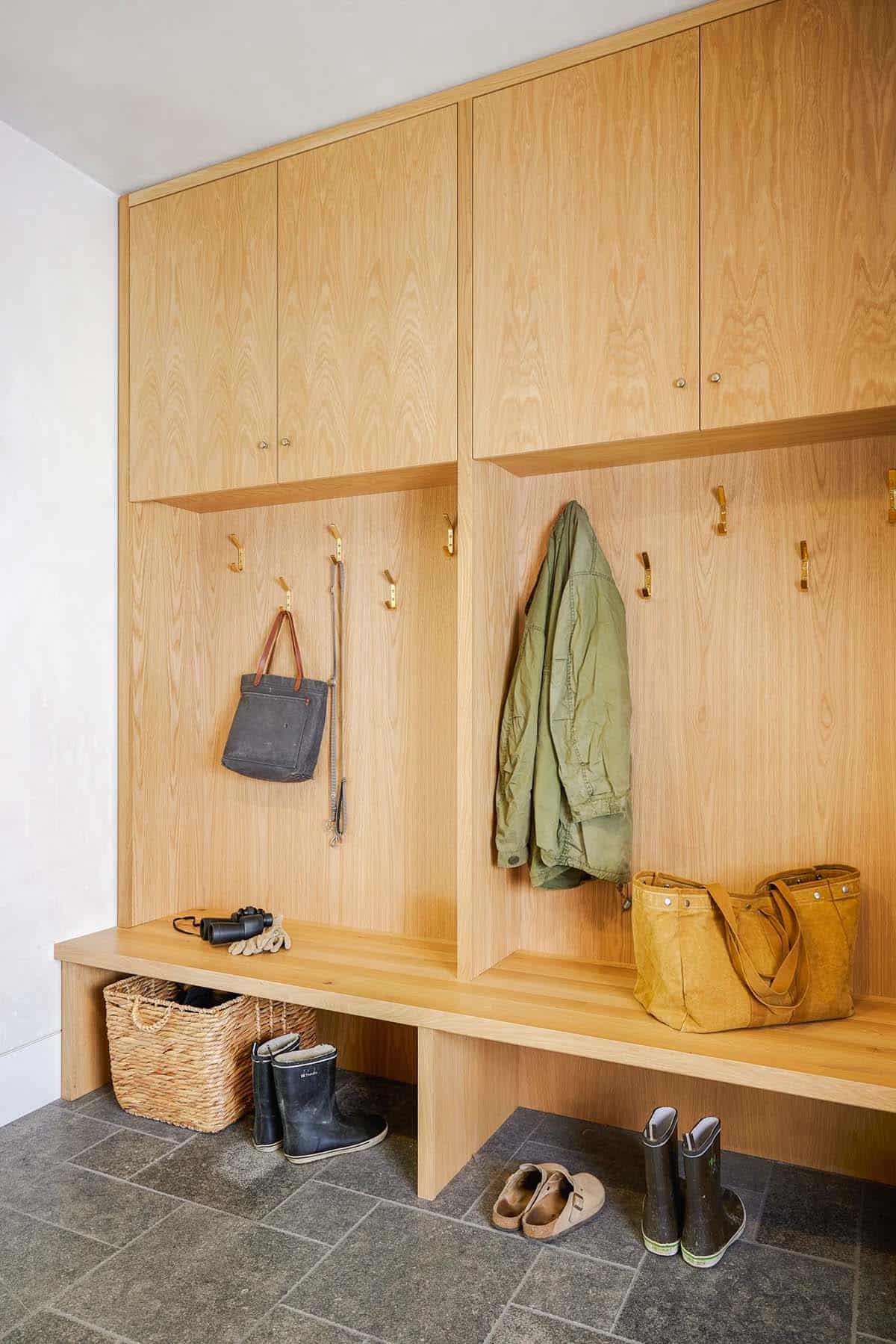 Oak mudroom with built-in cabinets, brass hooks, and slate floor