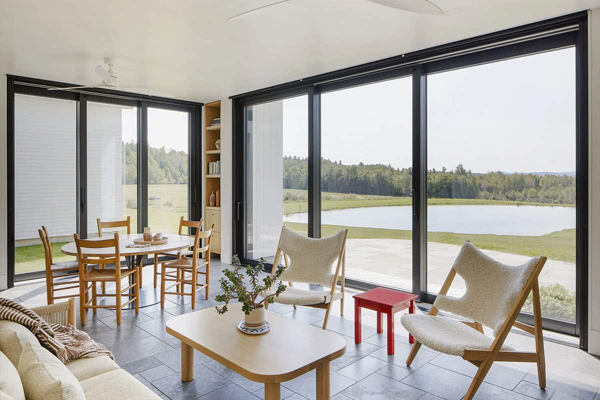 Sunroom with sliding glass walls, sheepskin chairs, and pond view