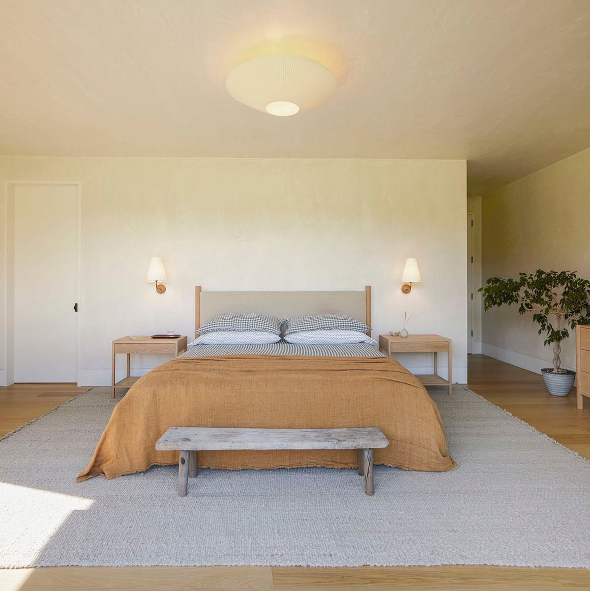 Primary bedroom with linen headboard, rustic bench, and pleated pendant light