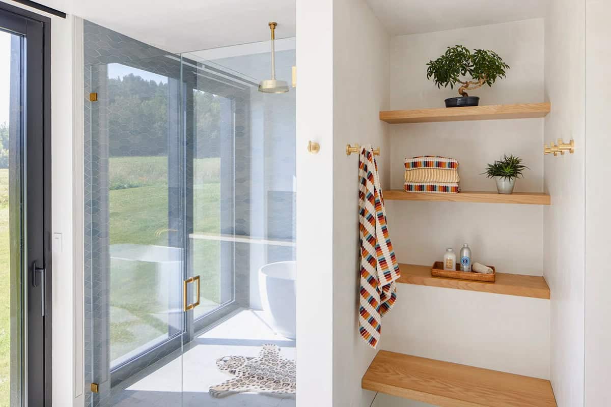 Bathroom with blue hexagon tile shower, oak shelving, and sliding glass door to the meadow
