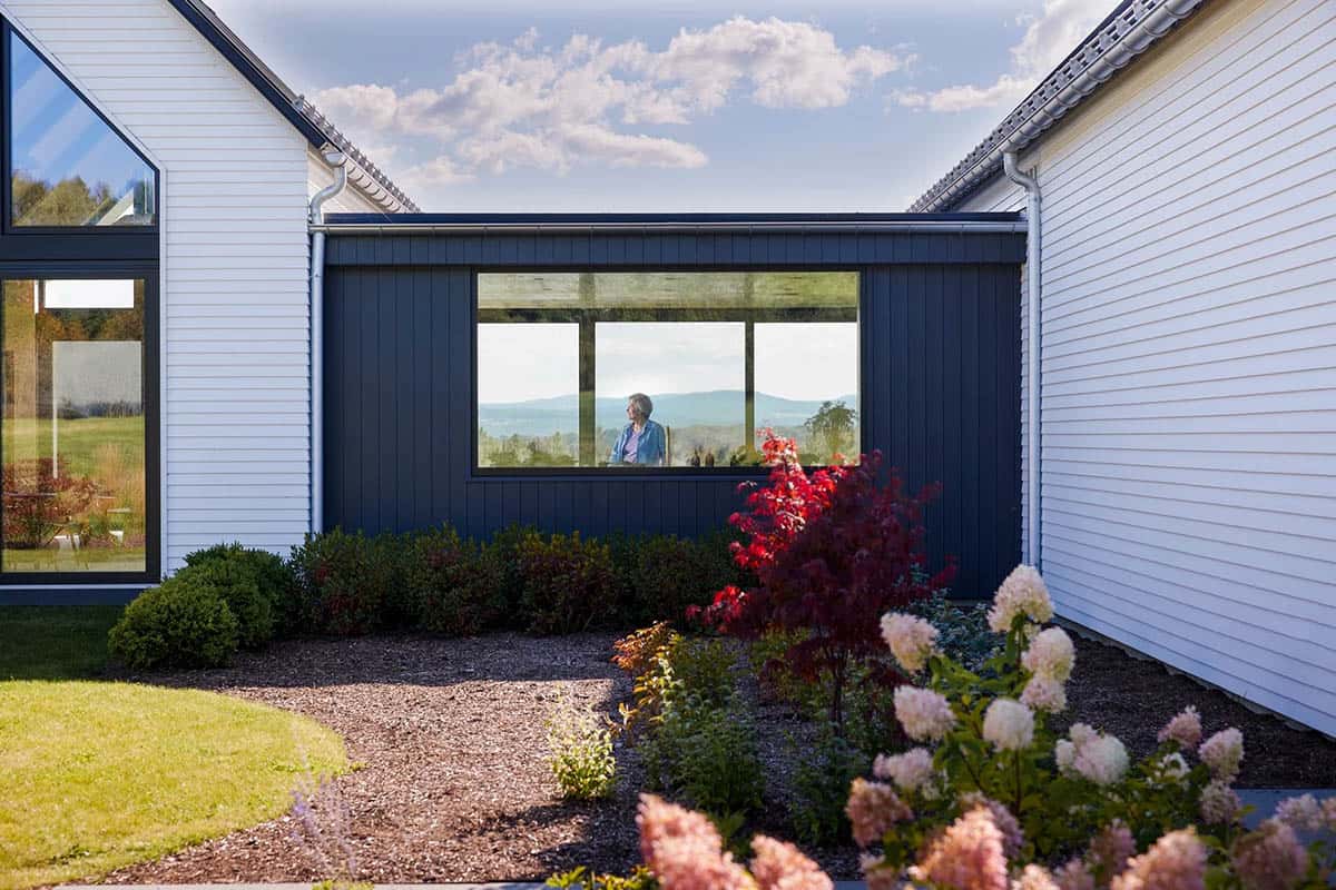 Courtyard between white gabled wings and a dark connector, with hydrangeas and a mountain view