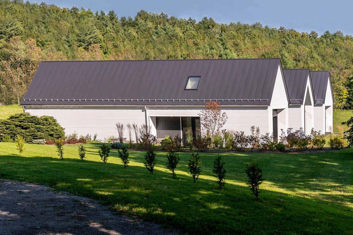 Side view of a long white clapboard farmhouse with dark standing-seam metal roof and skylight