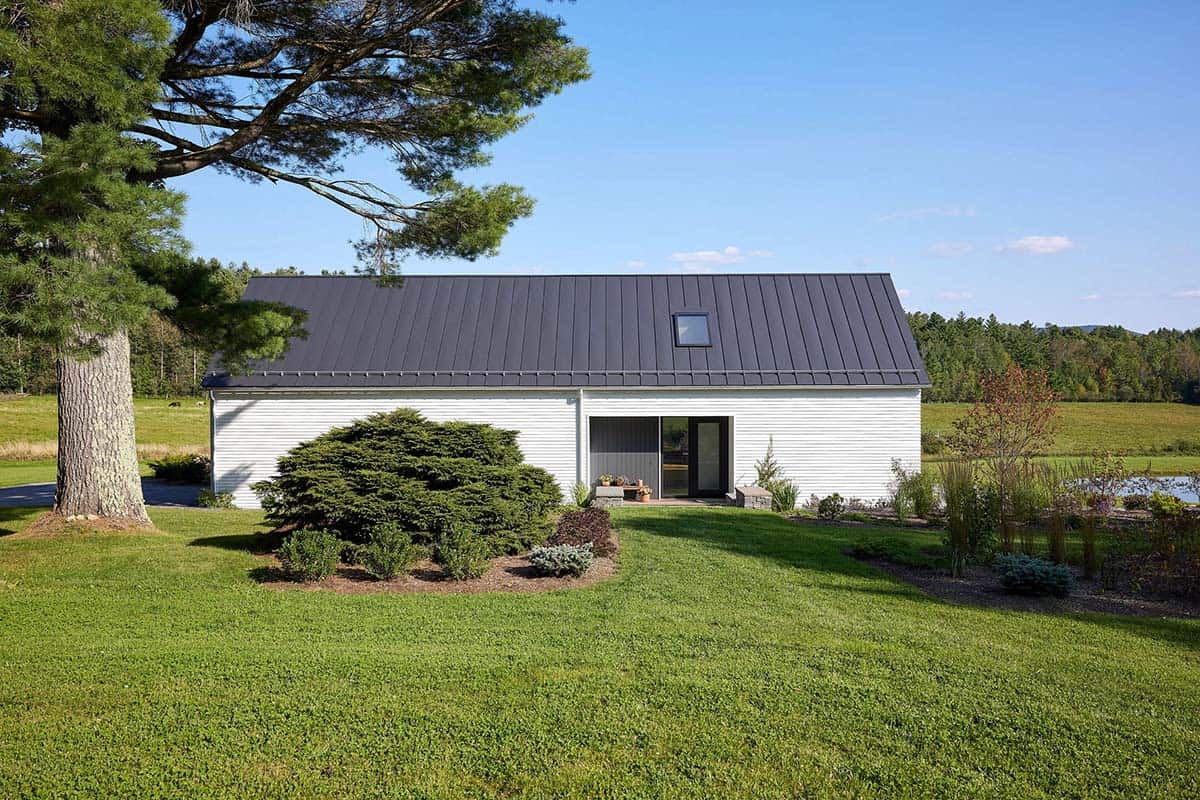 White gabled farmhouse wing with dark standing-seam metal roof, skylight, and mature pine tree
