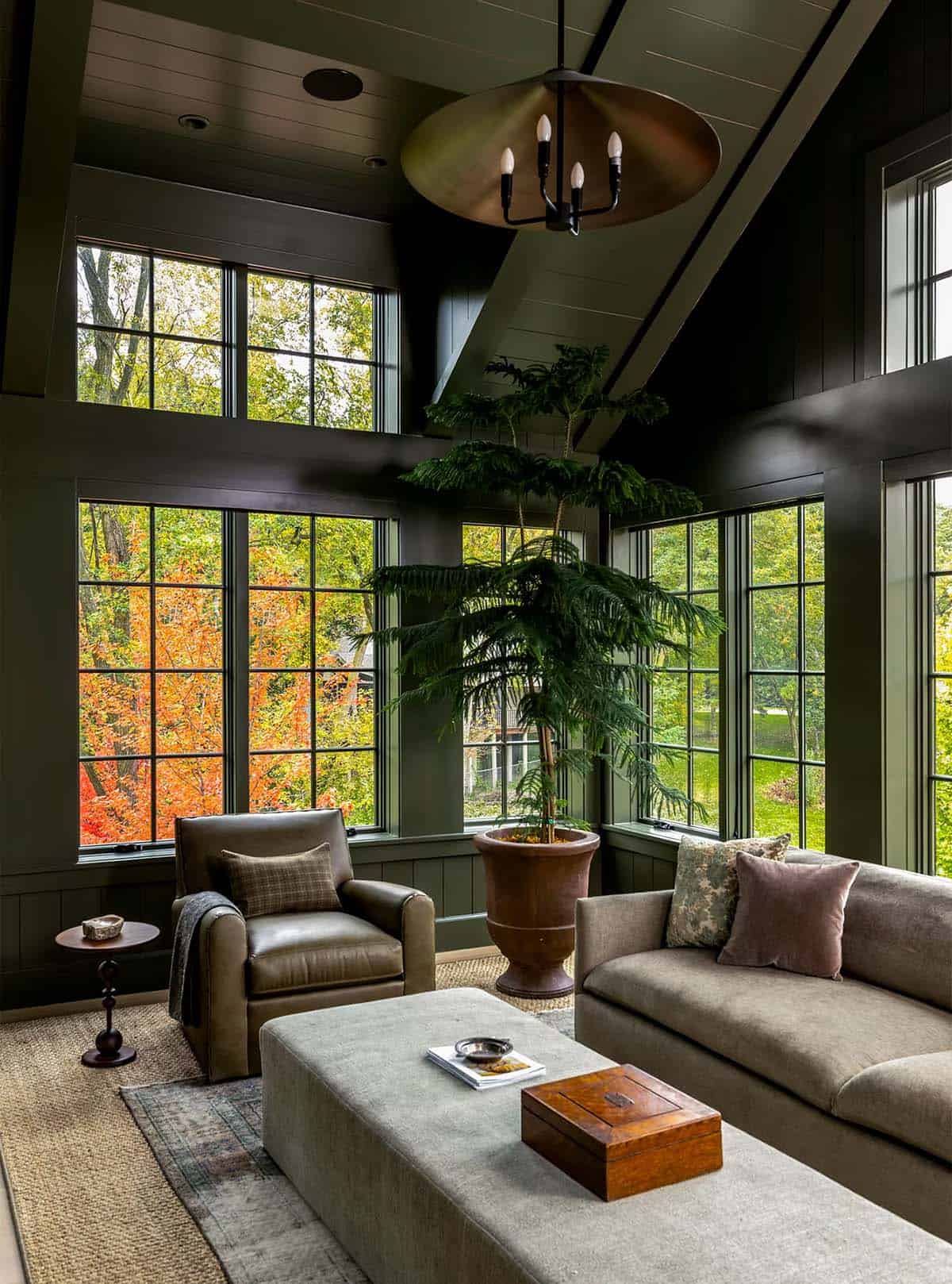 Corner of a green family room with a Norfolk pine in a terracotta urn, a leather club chair and a brass dish pendant under a vaulted paneled ceiling