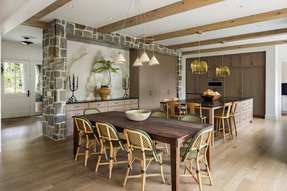 Dining area with a walnut table, green and natural rattan bistro chairs and a stone-framed niche holding a veined marble slab above an oak buffet