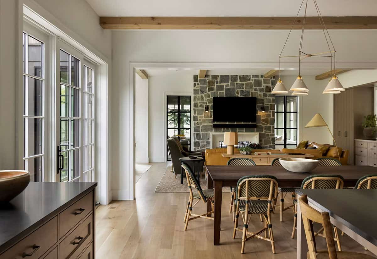View from the kitchen island past the dining table to the living room's stone fireplace, with white French doors on the left