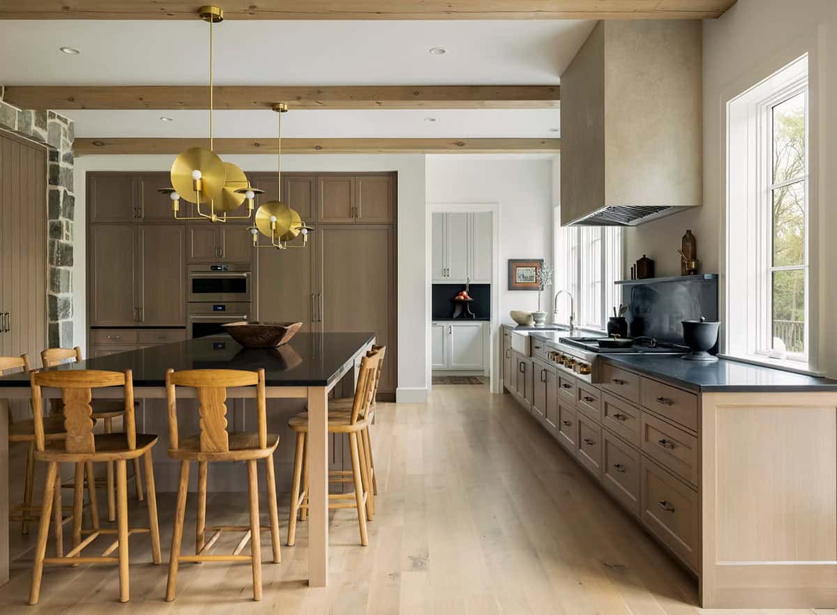 Kitchen with warm oak cabinetry, a black-topped island with carved wood counter stools, brass disc pendants and a plaster range hood
