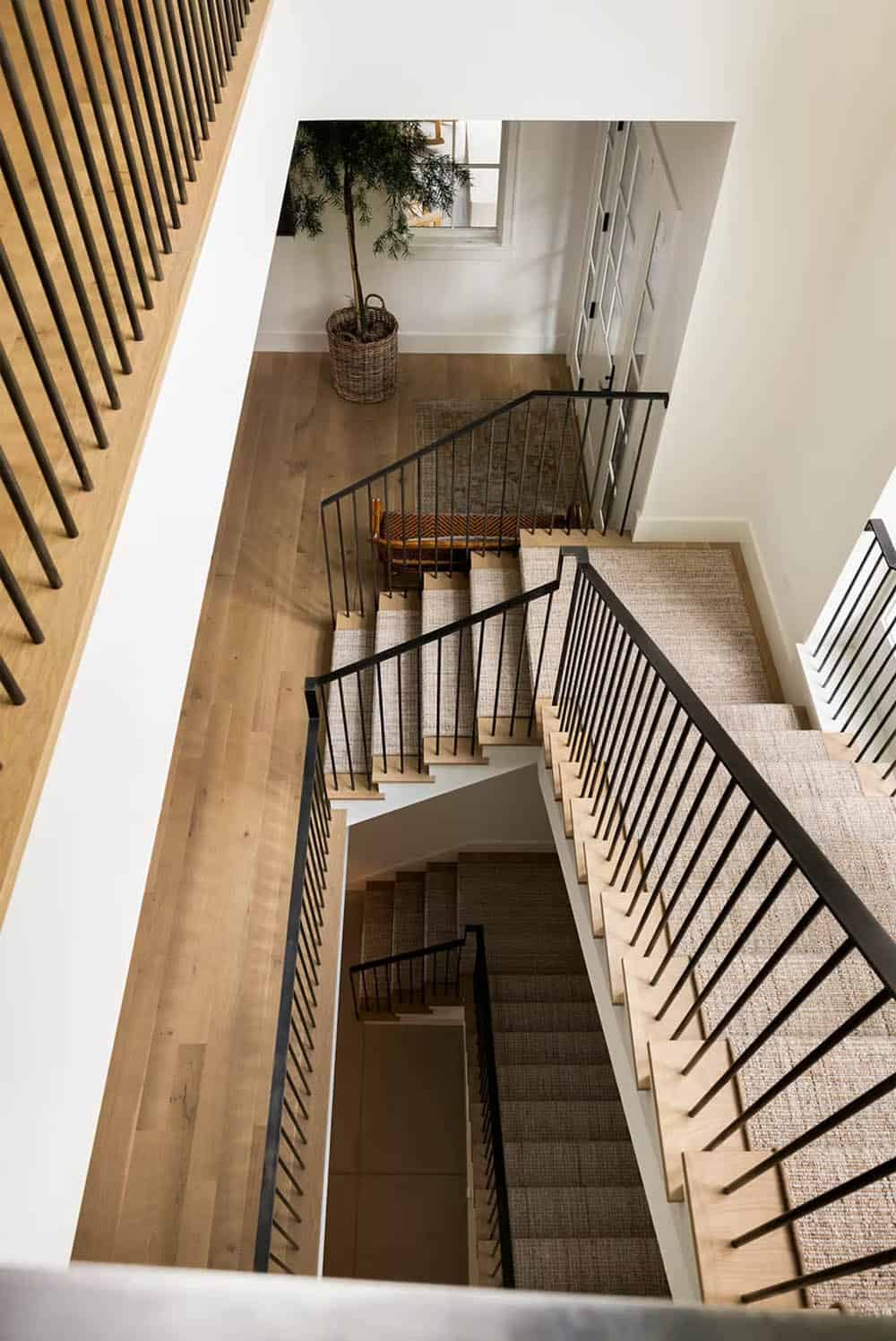 Overhead view down a switchback staircase with woven runners, light wood treads and slender black metal balusters