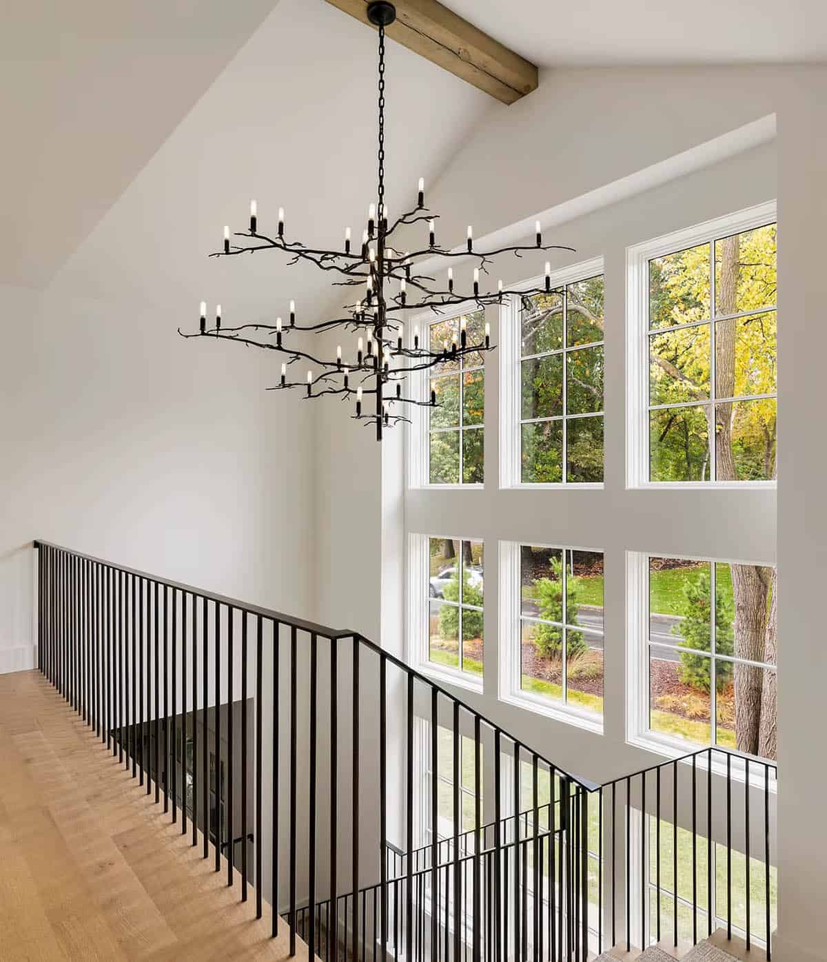 Upper stair landing with a black branch chandelier beneath a vaulted ceiling and two stories of white-framed windows