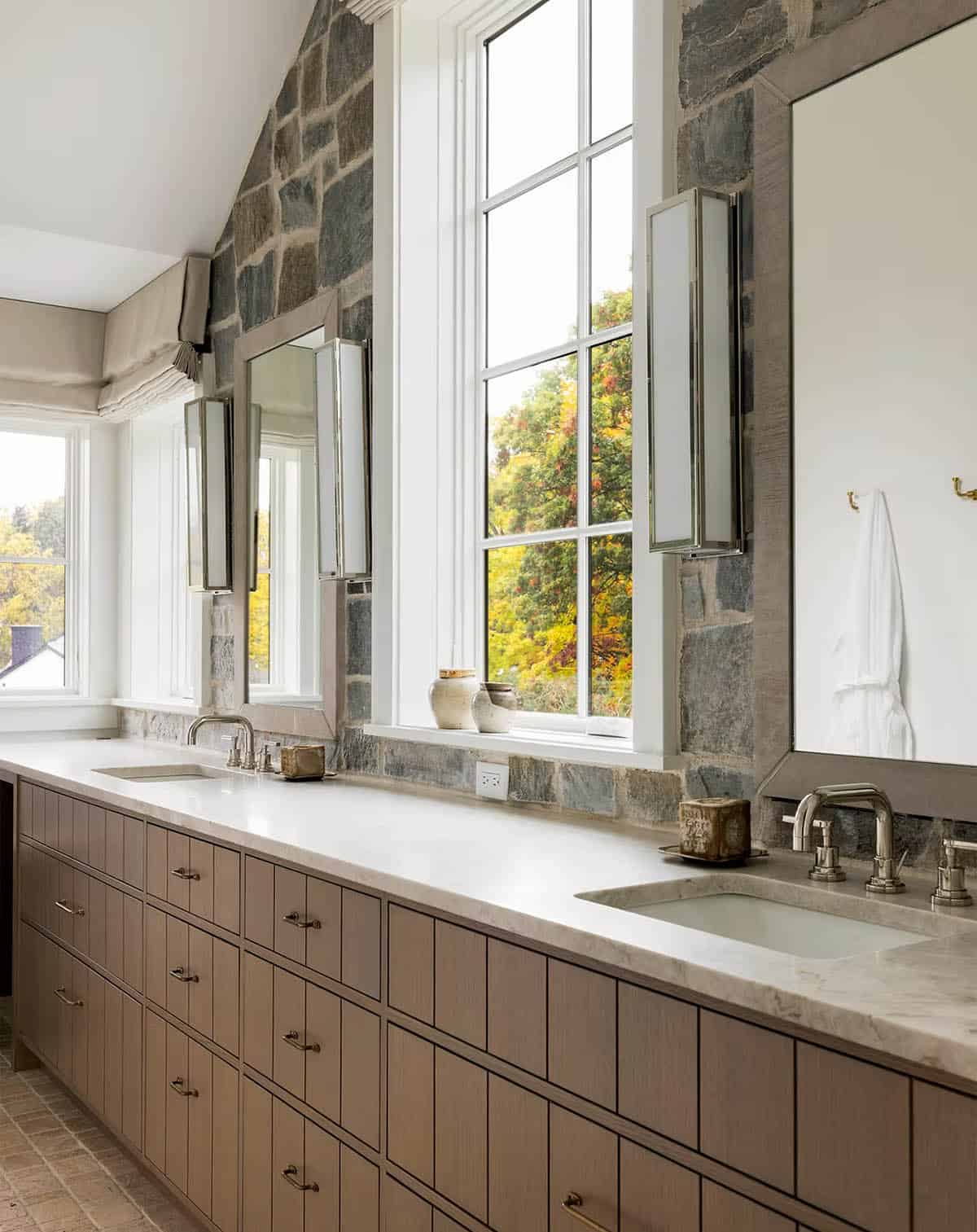 Primary bathroom with a long grooved oak double vanity, a cream stone countertop, polished nickel fixtures and a natural stone accent wall