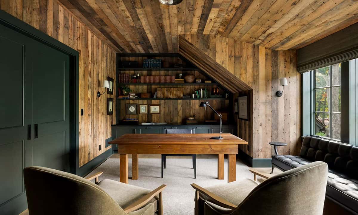 Home office clad in reclaimed barnwood walls and ceiling, with dark green built-in shelves, a wood desk and olive mohair lounge chairs